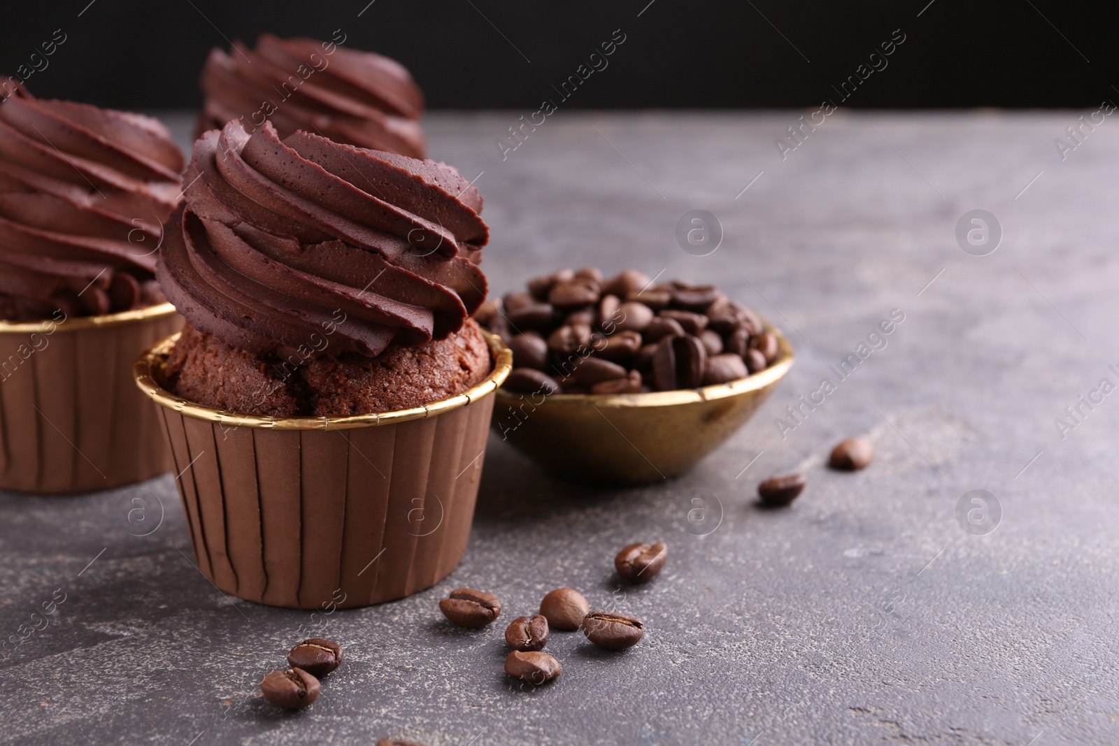 Photo of Delicious chocolate cupcakes and coffee beans on grey textured table, closeup. Space for text