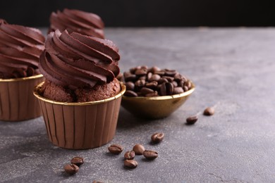 Delicious chocolate cupcakes and coffee beans on grey textured table, closeup. Space for text