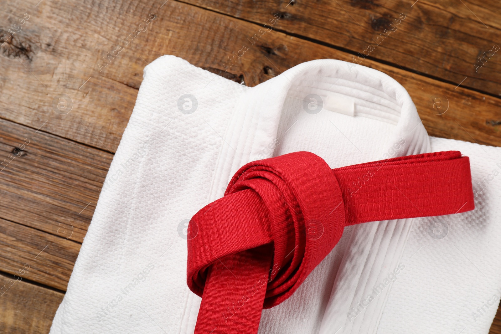 Photo of Red karate belt and white kimono on wooden background, top view