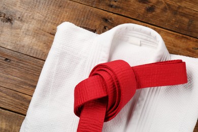 Red karate belt and white kimono on wooden background, top view