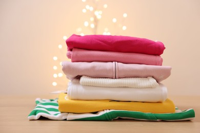 Photo of Stack of folded clothes on wooden table against beige background with blurred lights