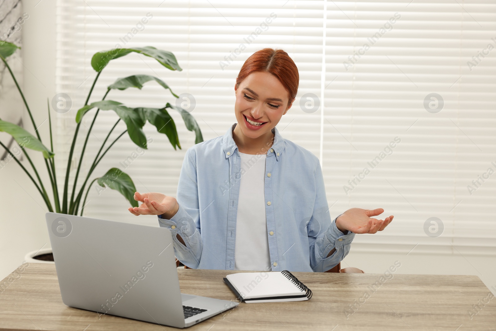 Photo of Young woman having video chat via laptop at wooden table indoors