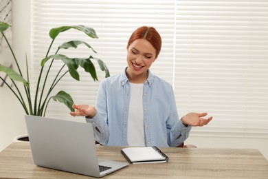 Young woman having video chat via laptop at wooden table indoors