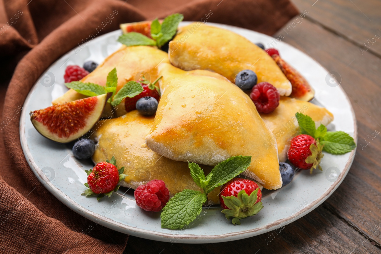 Photo of Delicious samosas with figs and berries on wooden table, closeup