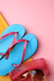 Photo of Light blue flip flops, sunglasses and case on pink background, top view with space for text. Beach accessories