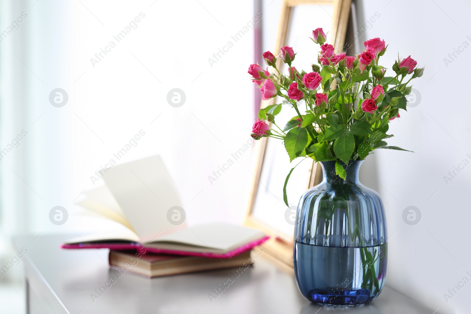 Photo of Glass vase with fresh flowers and books on grey table