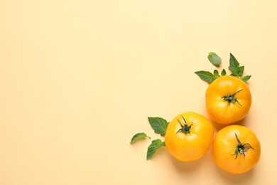 Photo of Fresh ripe yellow tomatoes and leaves on beige background, flat lay. Space for text