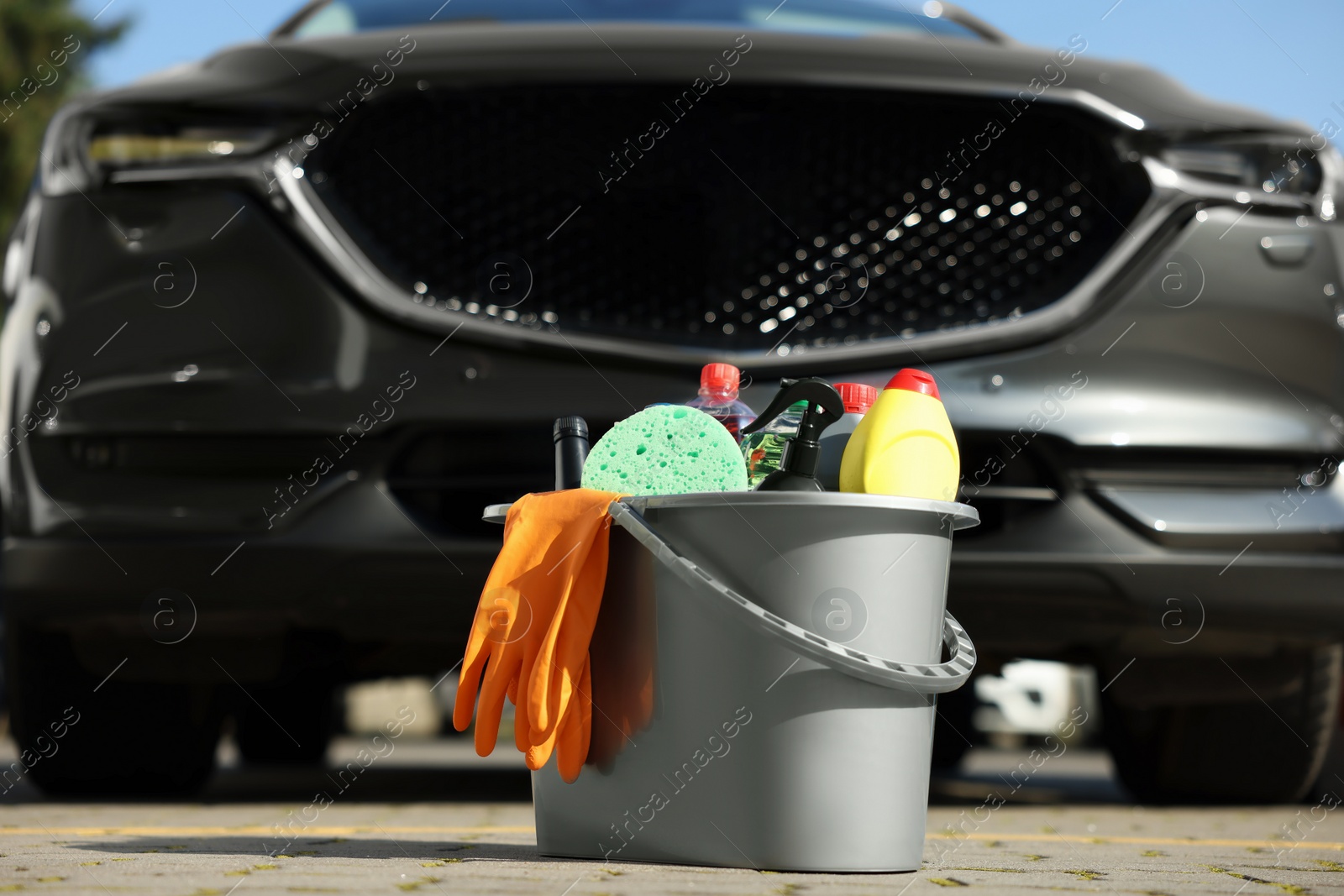 Photo of Car cleaning products in bucket near automobile outdoors on sunny day
