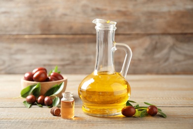 Glass jug with jojoba oil and seeds on wooden table