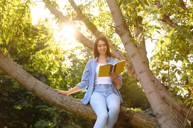 Photo of Young woman reading book on tree in park