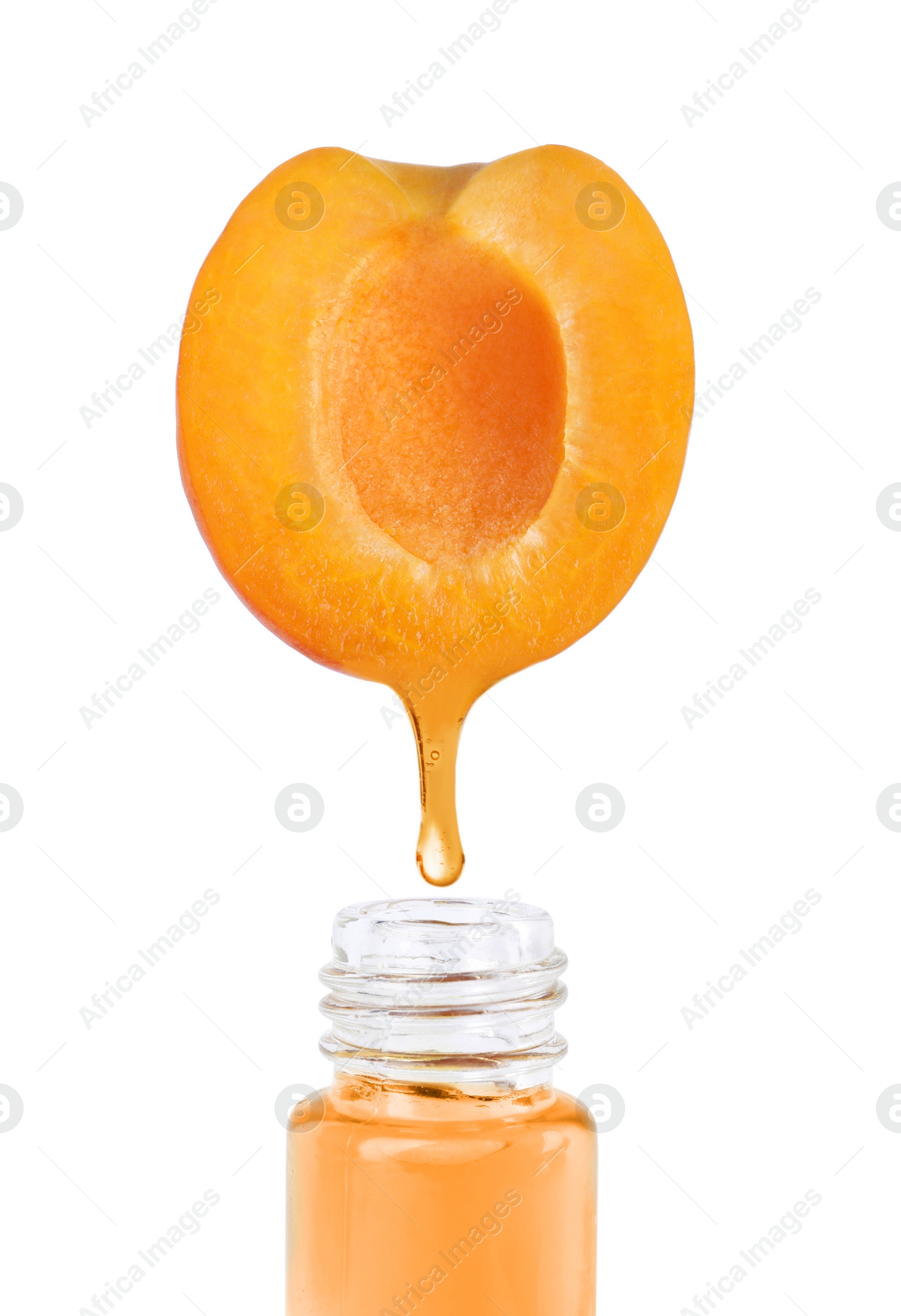 Image of Apricot oil dripping from fresh fruit half into glass bottle on white background