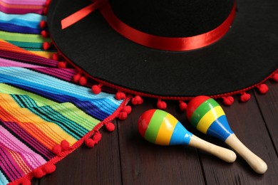 Photo of Mexican sombrero hat, maracas and colorful poncho on wooden background