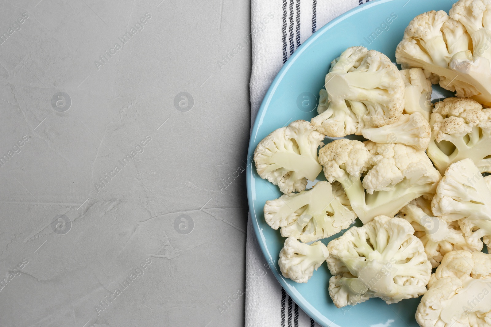 Photo of Plate with cut fresh raw cauliflower on light grey table, top view. Space for text