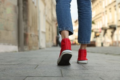 Photo of Woman in stylish sneakers walking on city street, closeup. Space for text