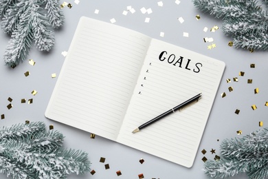 Photo of Word Goals written in notebook surrounded by Christmas decor on light grey background, flat lay
