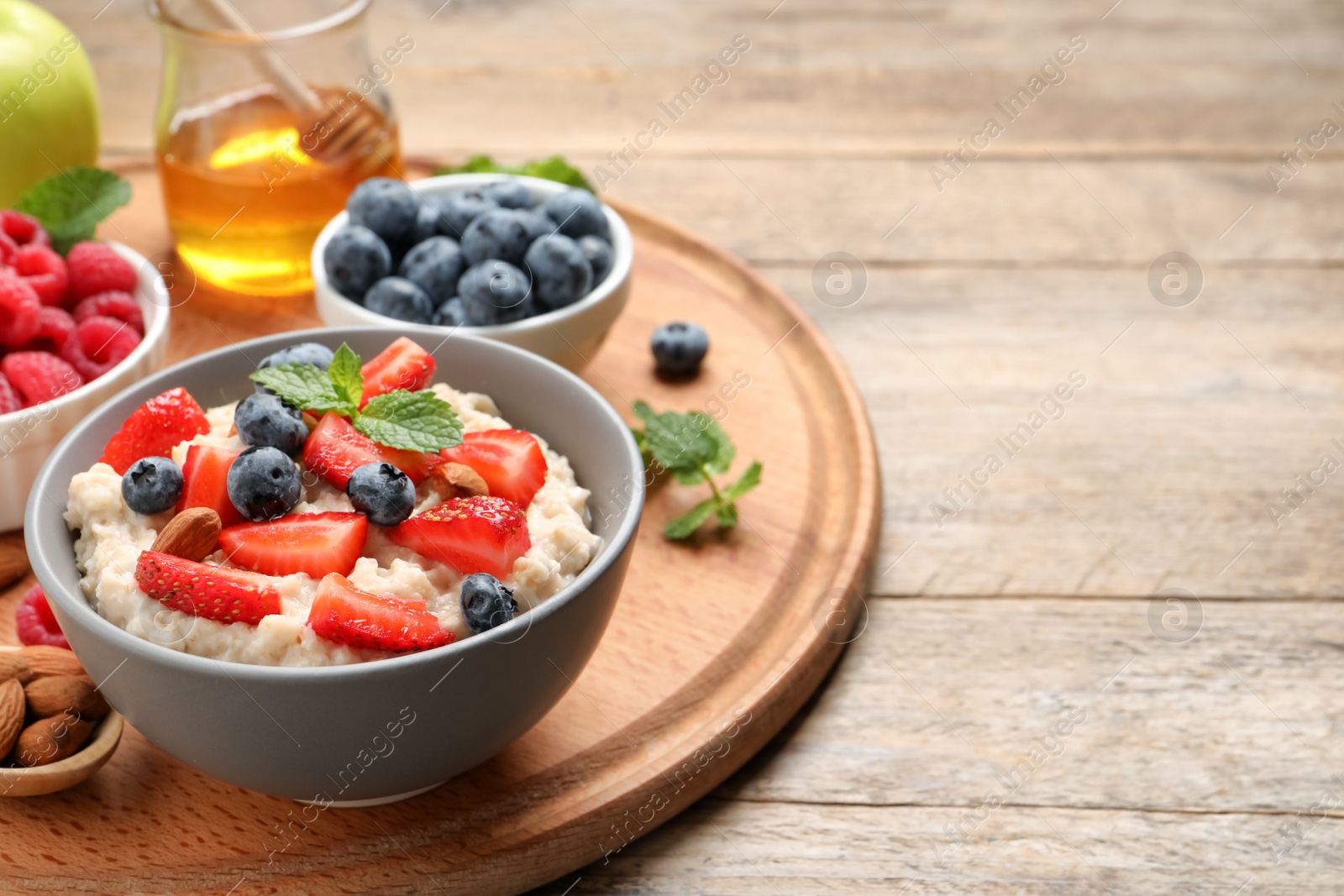 Photo of Tasty oatmeal porridge with berries and almond nuts served on wooden table, space for text