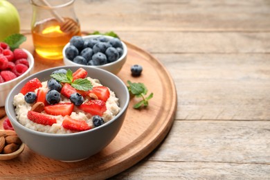 Photo of Tasty oatmeal porridge with berries and almond nuts served on wooden table, space for text