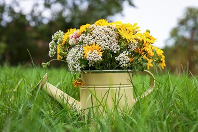 Photo of Pale yellow watering can with beautiful flowers on green grass outdoors