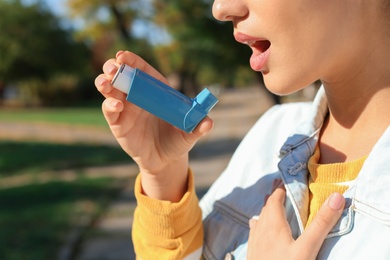 Photo of Woman using asthma inhaler outdoors. Health care