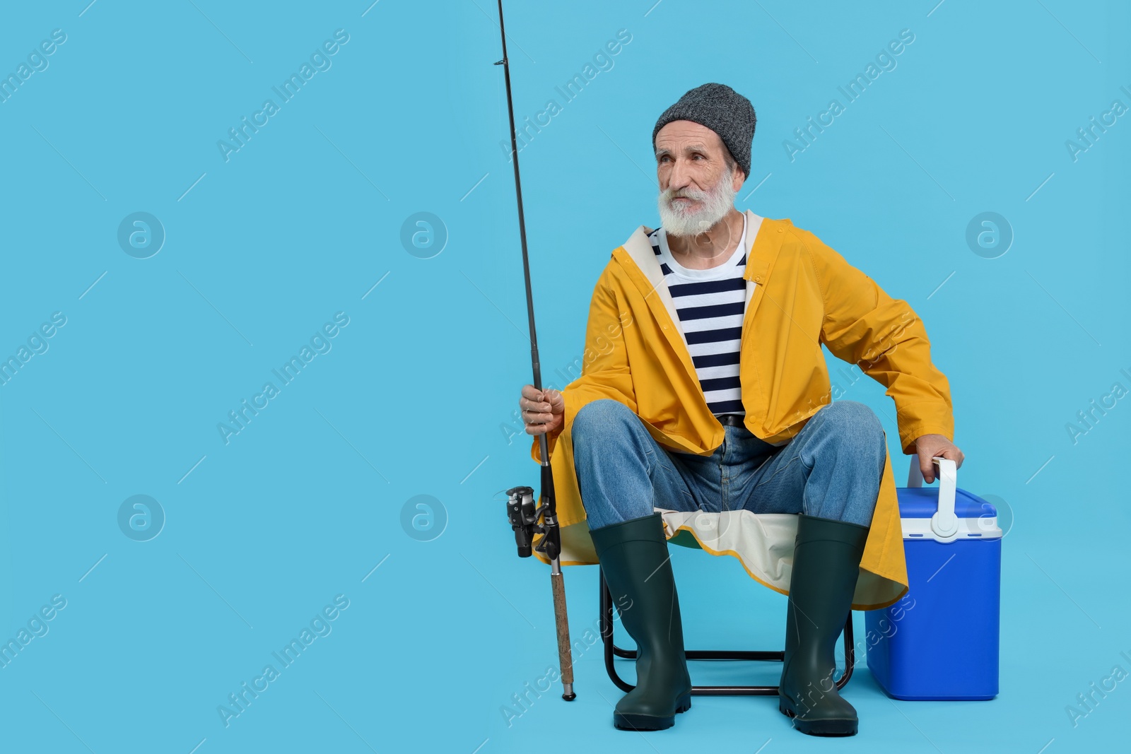 Photo of Fisherman with rod and cool box on chair against light blue background, space for text