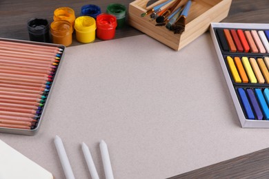 Photo of Blank sheet of paper, colorful chalk pastels and other drawing tools on wooden table. Modern artist's workplace