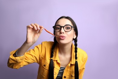 Photo of Fashionable young woman with braids chewing bubblegum on lilac background