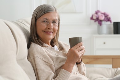 Photo of Beautiful senior woman with cup of drink on sofa at home