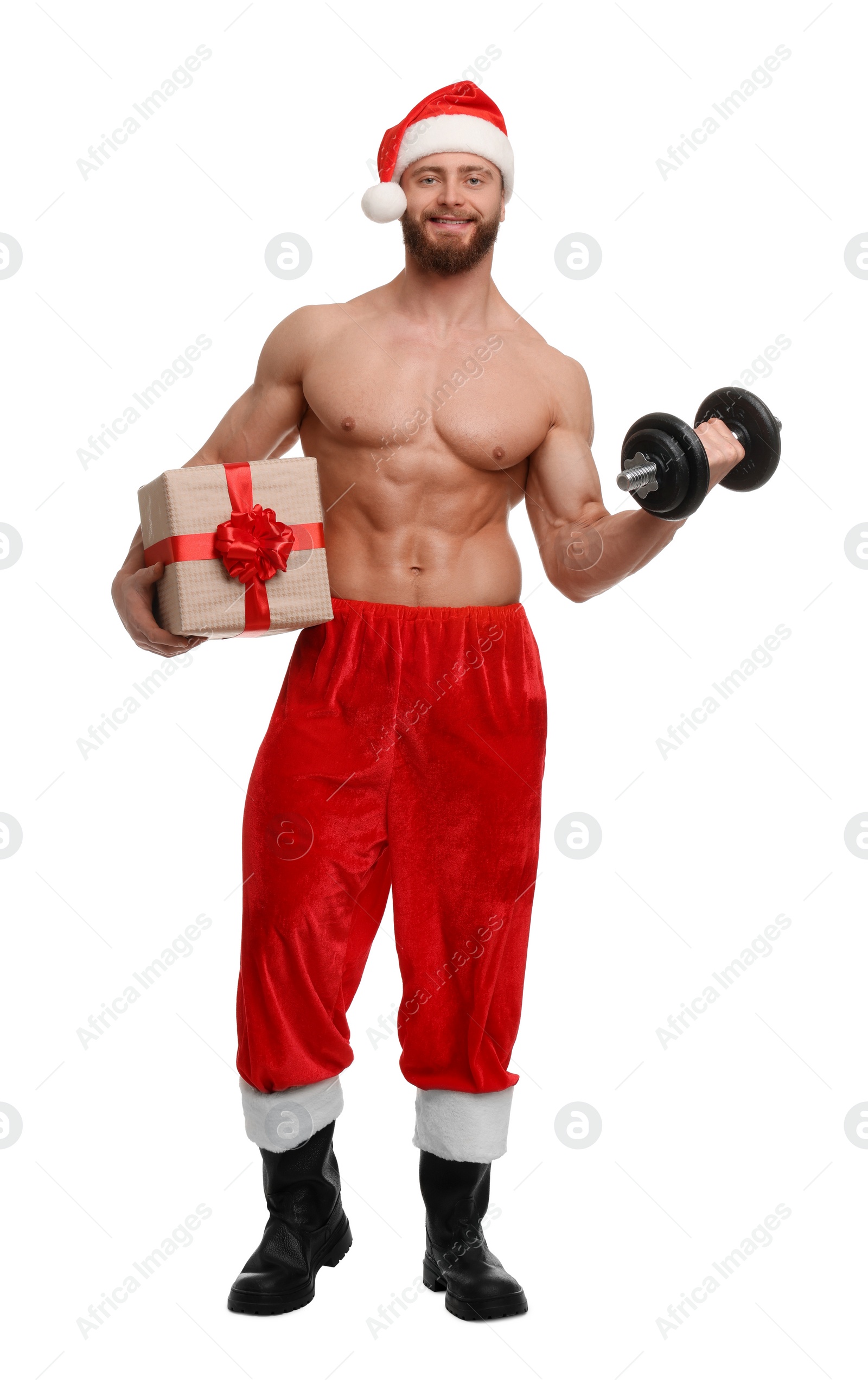 Photo of Attractive young man with muscular body in Santa hat holding Christmas gift box and dumbbell on white background