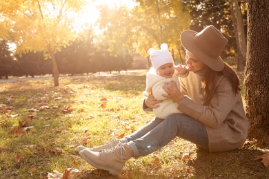 Photo of Happy mother with her baby daughter sitting near tree in park on sunny autumn day, space for text