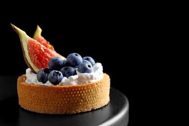 Photo of Tart with blueberries and figs on black table against dark background, space for text. Delicious pastries