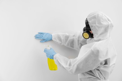 Photo of Woman in protective suit cleaning mold with sprayer on wall