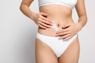 Photo of Woman with body cream smear on belly against light grey background, closeup. Space for text