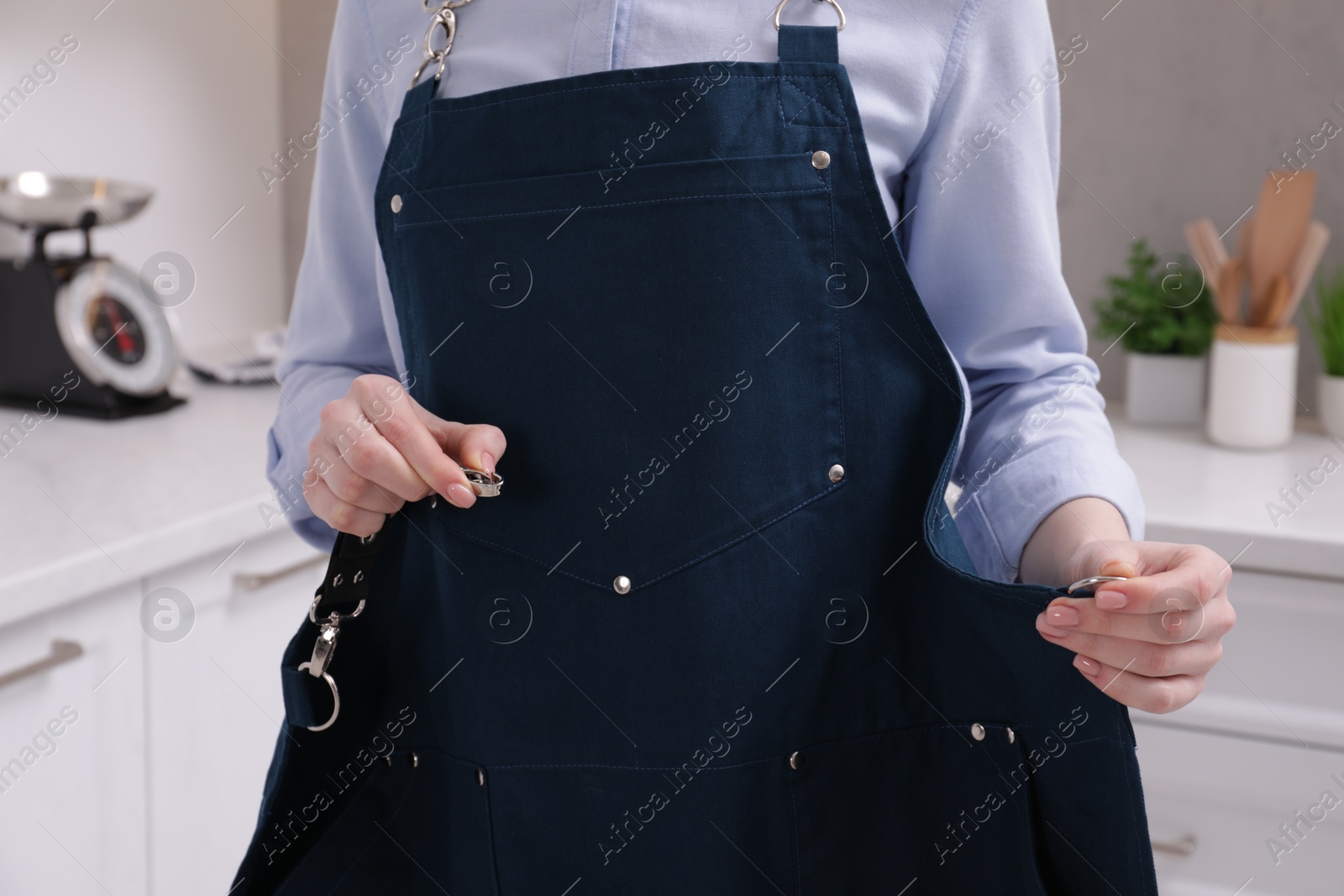 Photo of Woman putting on apron in kitchen , closeup