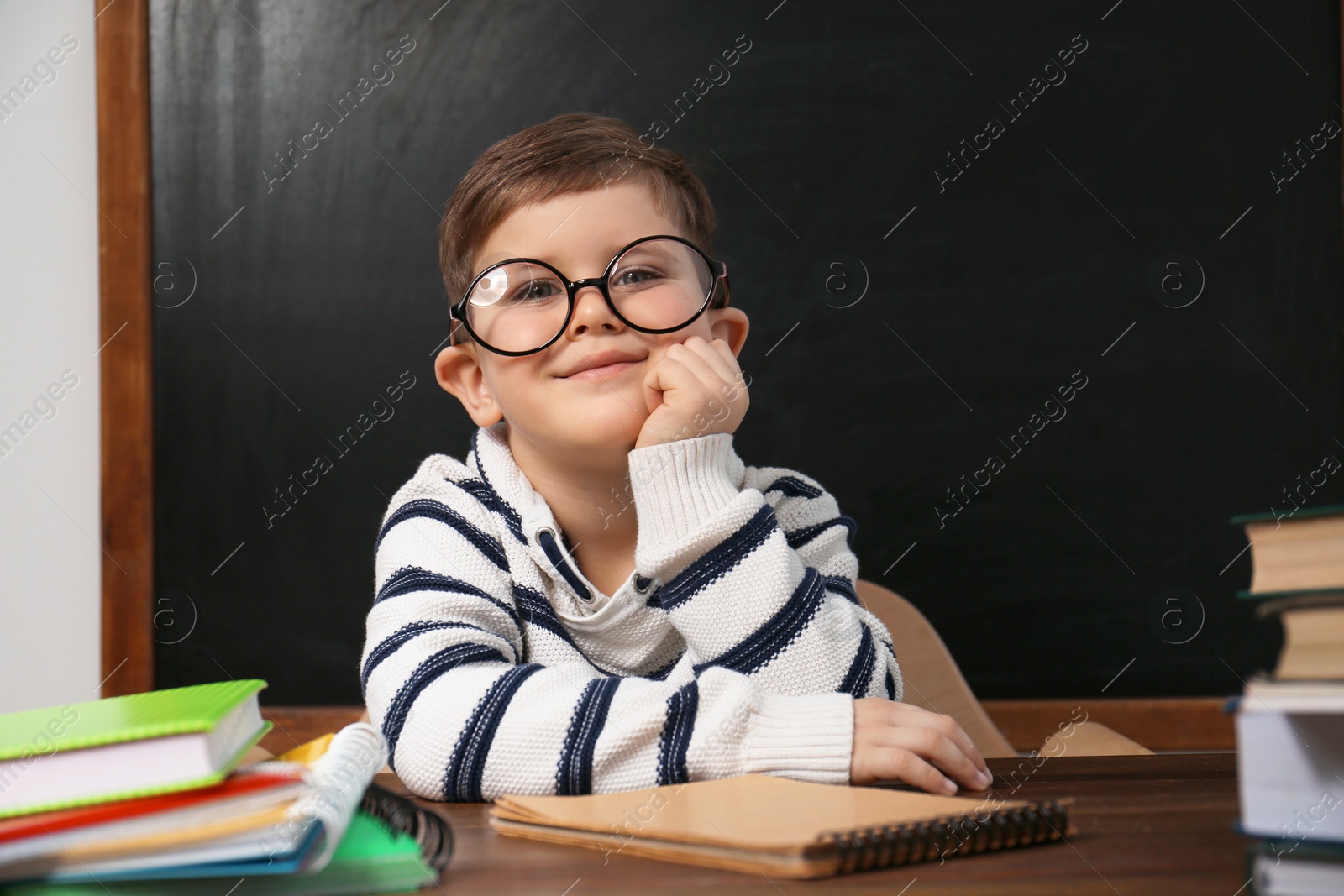 Photo of Cute little child wearing glasses at desk in classroom. First time at school