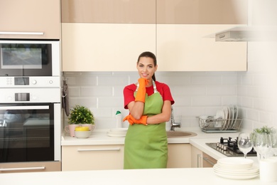 Photo of Beautiful young woman wearing gloves and apron in clean kitchen. Dish washing
