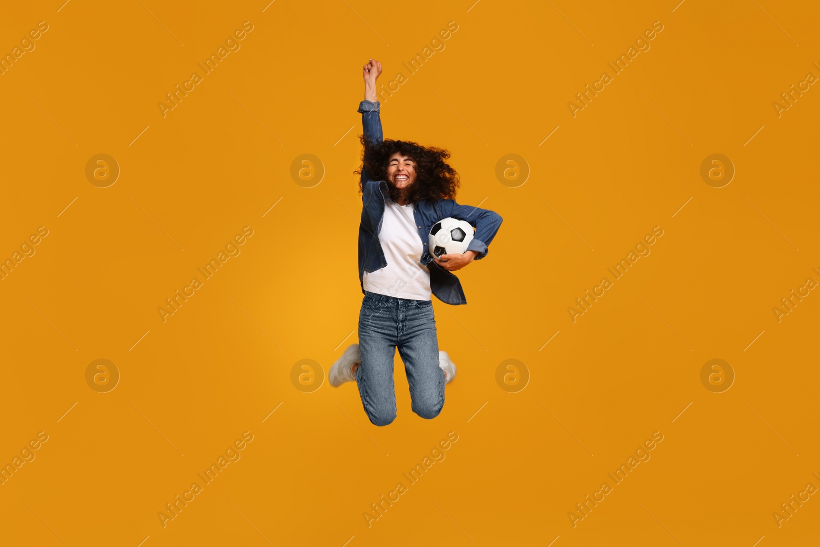 Photo of Happy fan with soccer ball jumping on yellow background