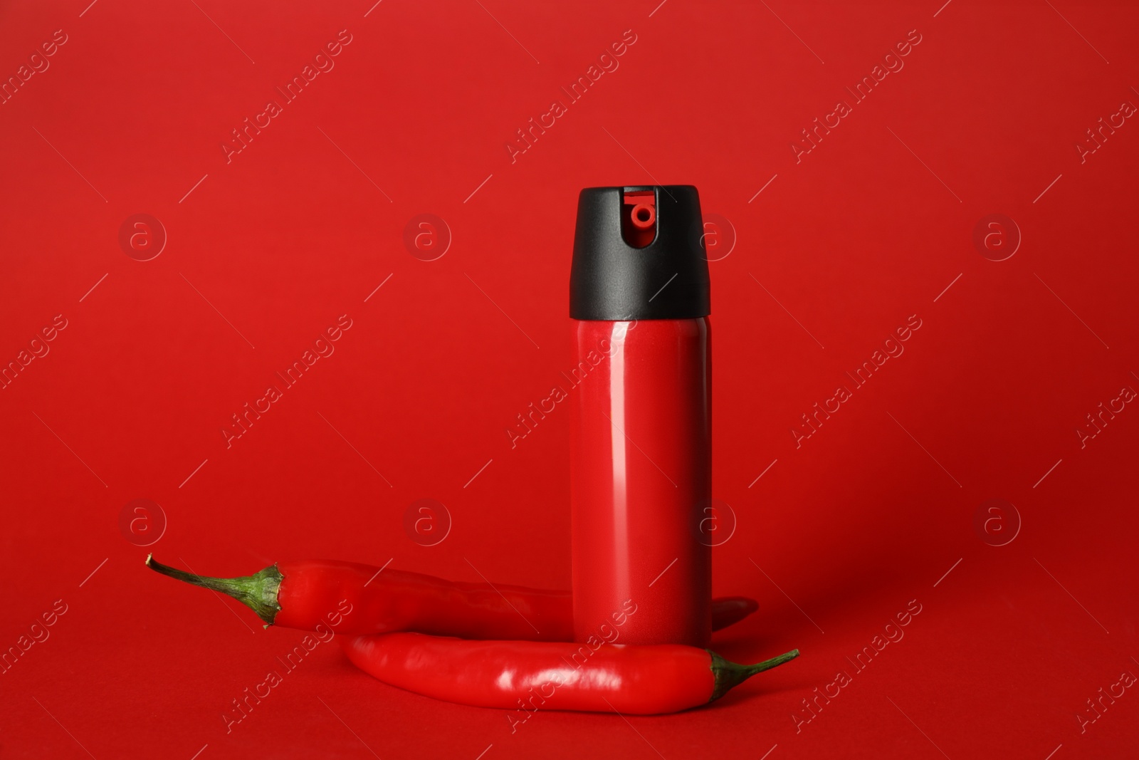 Photo of Bottle of gas pepper spray and fresh chili peppers on red background