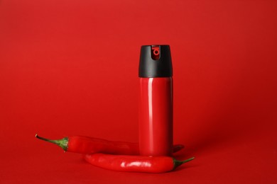 Photo of Bottle of gas pepper spray and fresh chili peppers on red background