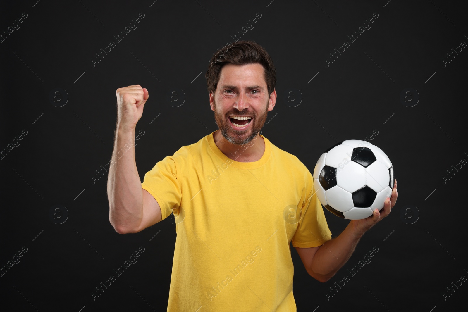 Photo of Emotional sports fan with soccer ball on black background