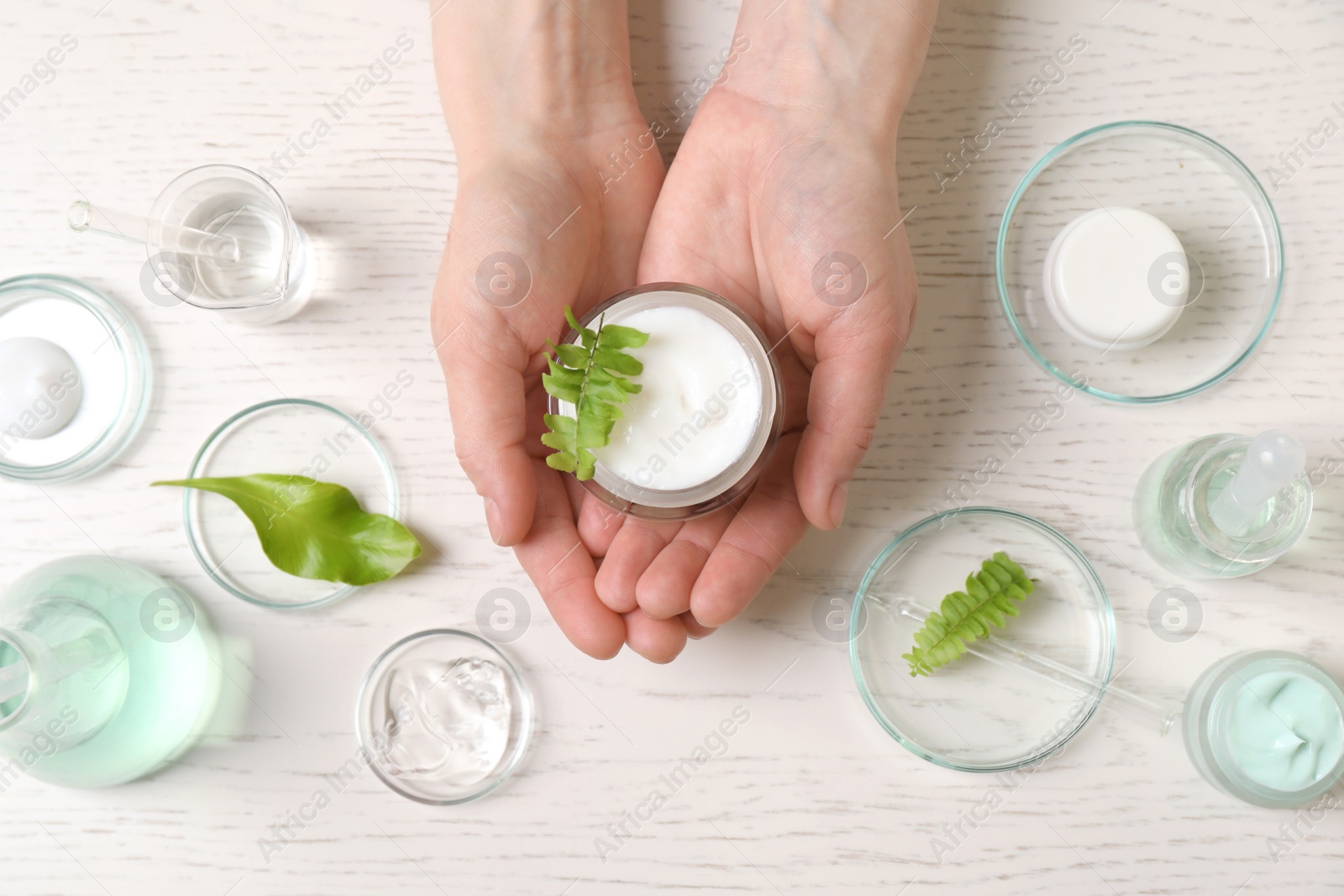 Photo of Woman holding jar of cosmetic product at white table, top view