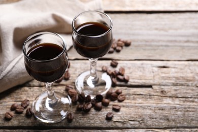 Photo of Glasses of coffee liqueur and beans on wooden table, space for text