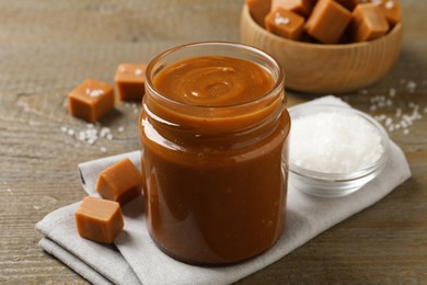 Photo of Yummy salted caramel in glass jar and candies on wooden table