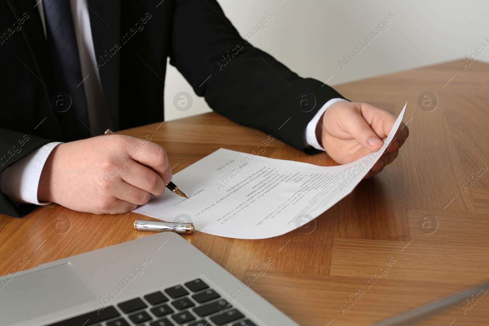 Photo of Notary signing document at wooden table, closeup