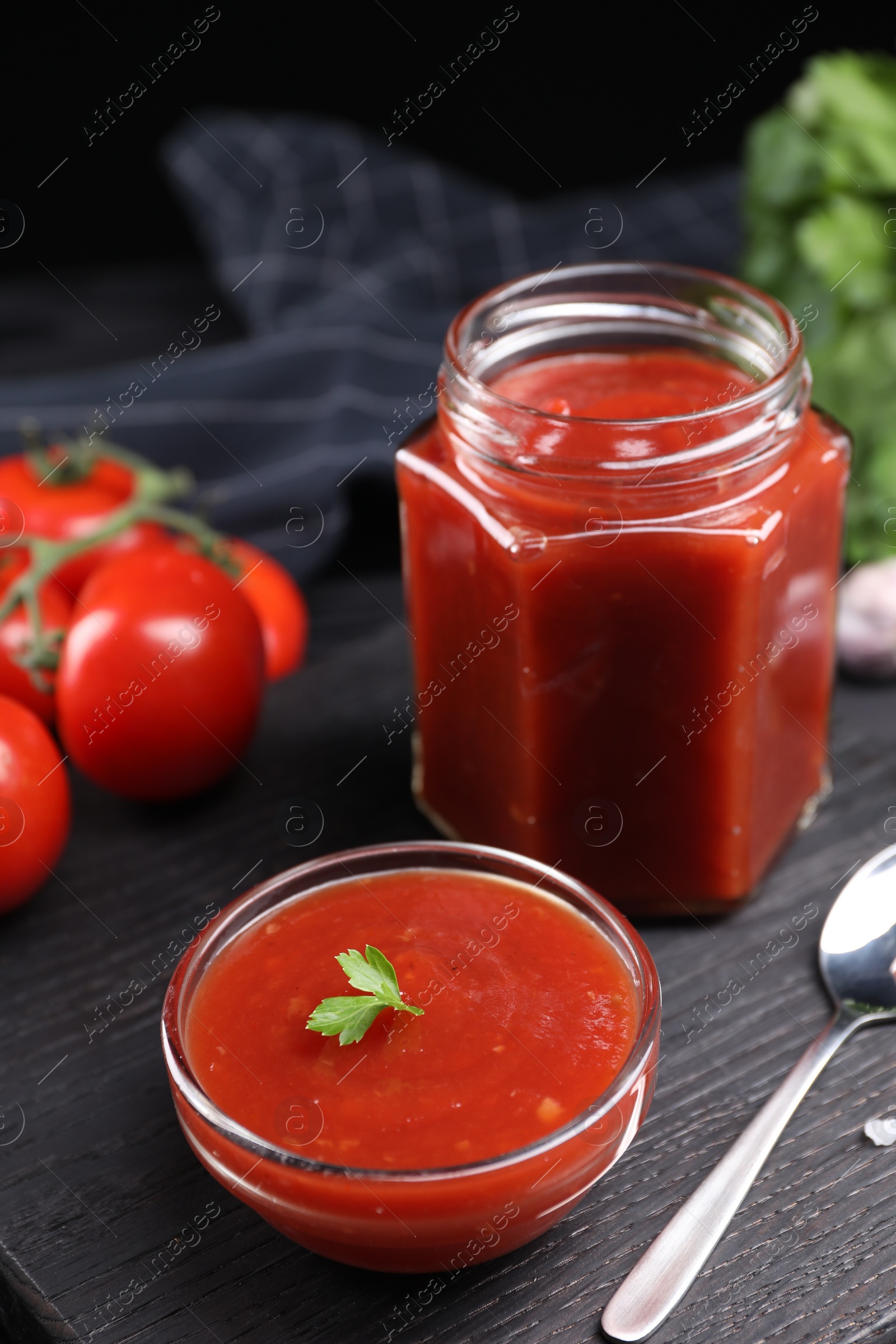 Photo of Delicious ketchup on black wooden table. Tomato sauce