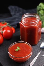 Photo of Delicious ketchup on black wooden table. Tomato sauce