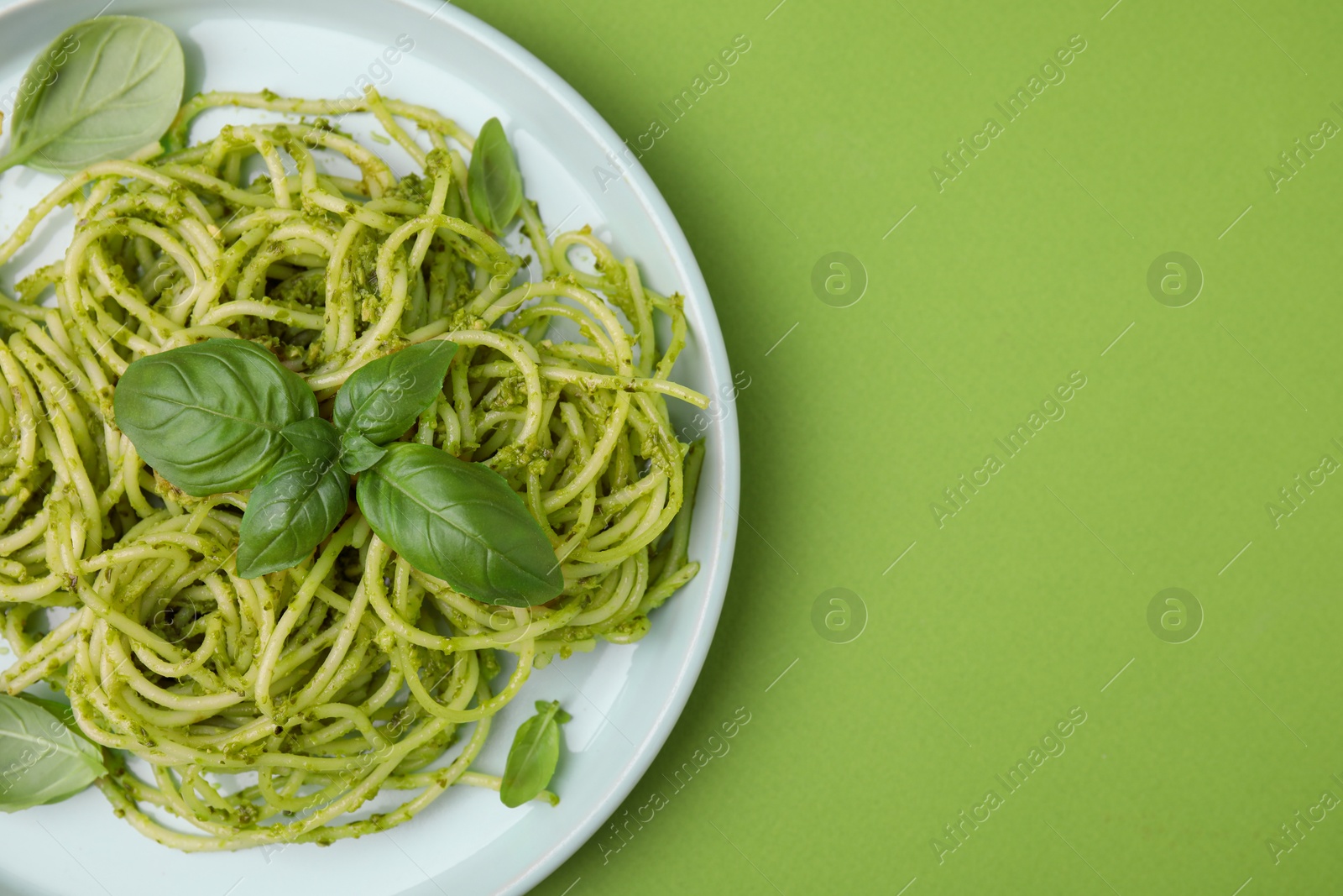 Photo of Delicious pasta with pesto sauce and basil on light green background, top view. Space for text