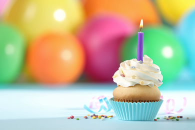 Photo of Birthday cupcake with candle and blurred balloons on background. Space for text