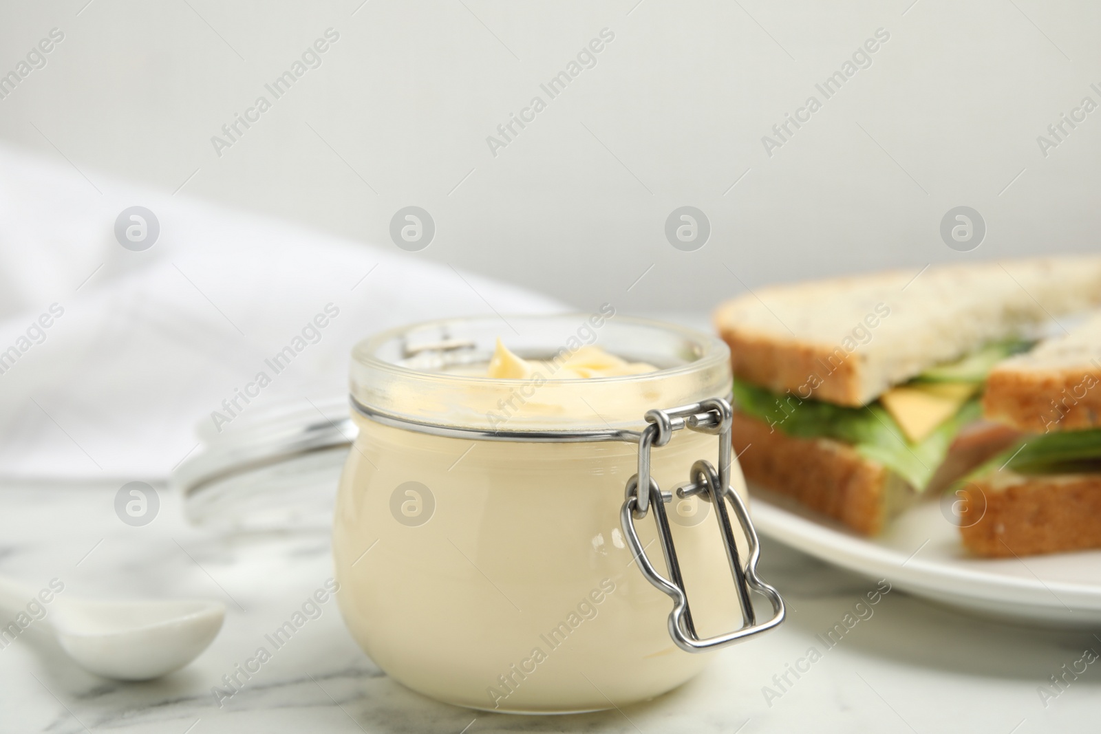 Photo of Jar of delicious mayonnaise near fresh sandwiches on white marble table