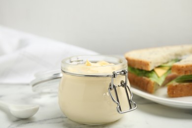 Jar of delicious mayonnaise near fresh sandwiches on white marble table