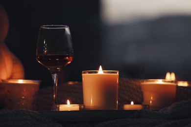 Photo of Glass of wine and burning candles near window indoors